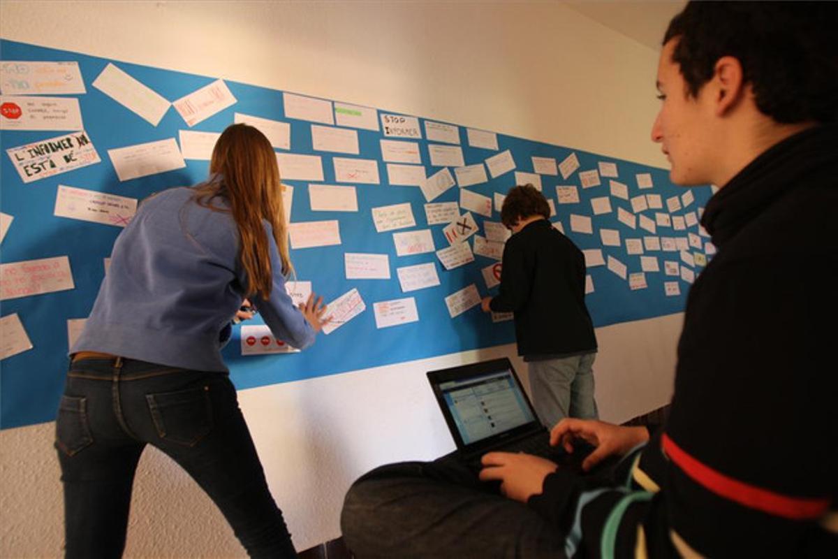Uns alumnes de l’escola Sadako enganxen en un mural missatges contra els rumors i un altre els tuiteja.