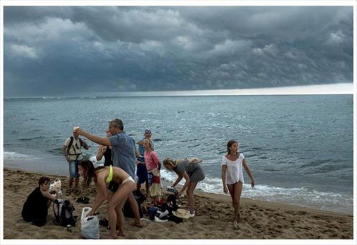 Uns banyistes recullen les coses a la platja de la Barceloneta després del sobtat ennegriment del cel, ahir.