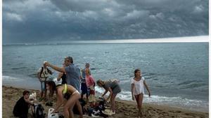 Uns banyistes recullen les coses a la platja de la Barceloneta després del sobtat ennegriment del cel, ahir.