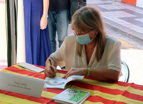 L'escriptora Vicky Carles signant exemplars del llibre 'La veu de les oliveres', amb alguns lectors esperant al darrera durant el Sant Jordi d'estiu a Tortosa.