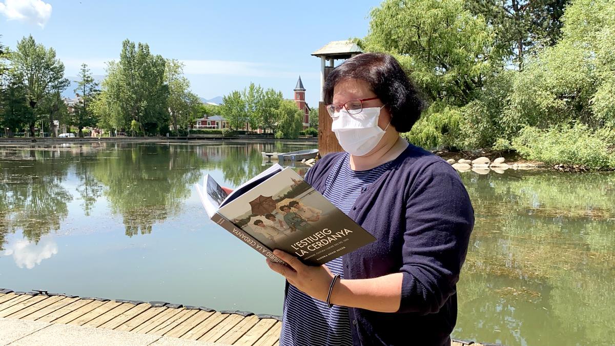 L&#039;escriptora Sandra Adam fullejant el seu nou llibre &#039;L&#039;estiueig a la Cerdanya&#039; amb el llac de Puigcerdà al fons