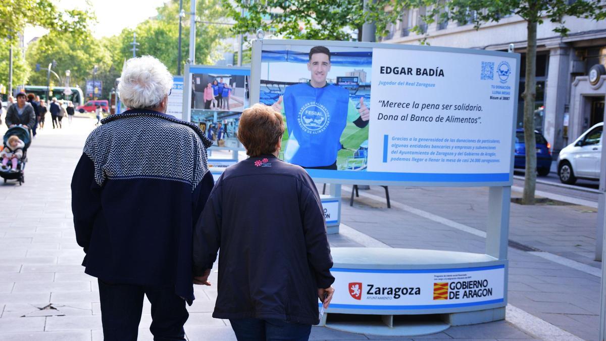 Una pareja observa a Edgar Badía, portero del Real Zaragoza, promocionando la Gran Recogida de mayo.