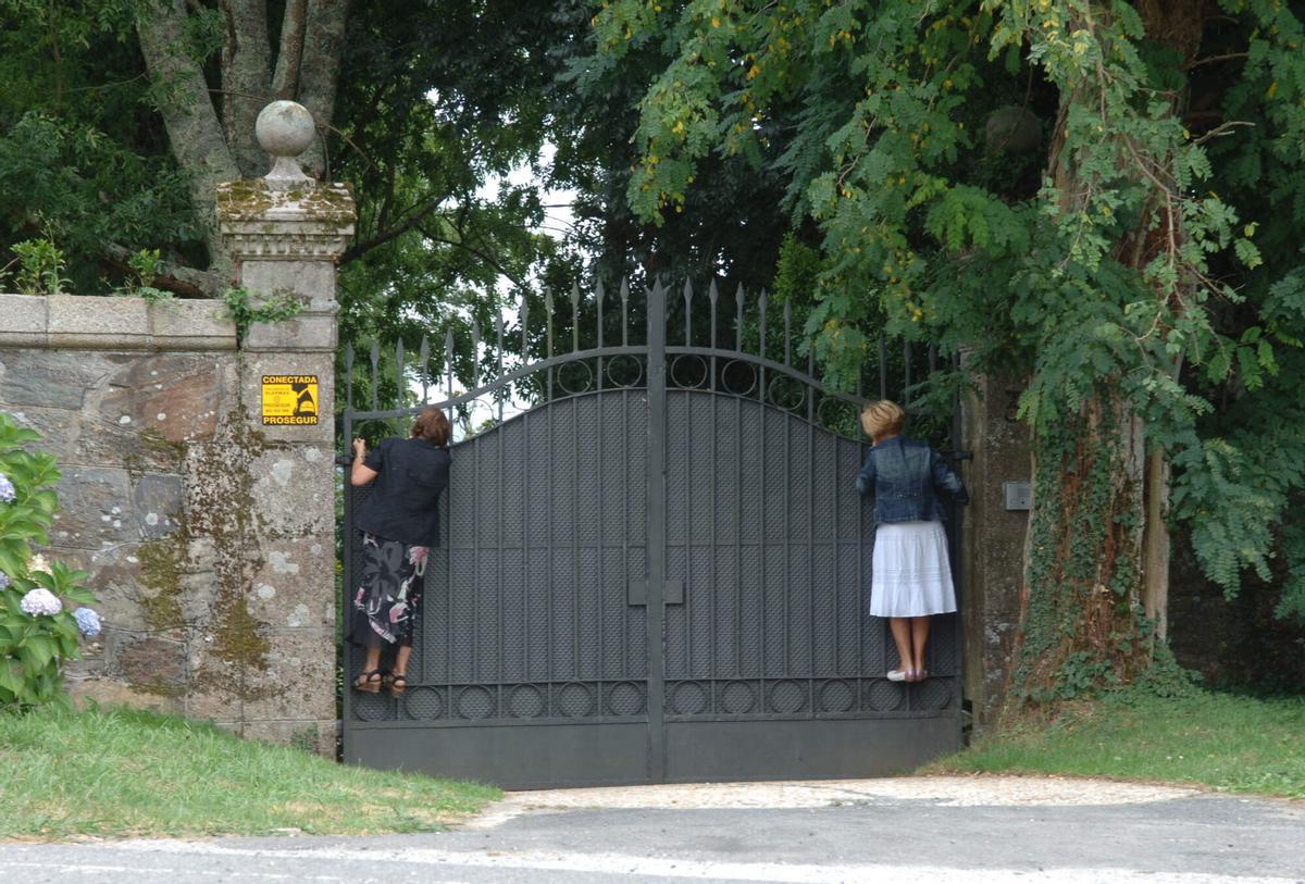 DOS MUJERES ENCARAMADAS AL PORTALON DE ENTRADA DEL PAZO DE MEIRAS PARA VER LOS JARDINES Y EL INMUEBLE, EN EL CONCELLO DE SADA. PAZOS. BIC. BIEN DE INTERES CULTURAL. VISITAS AL PUBLICO