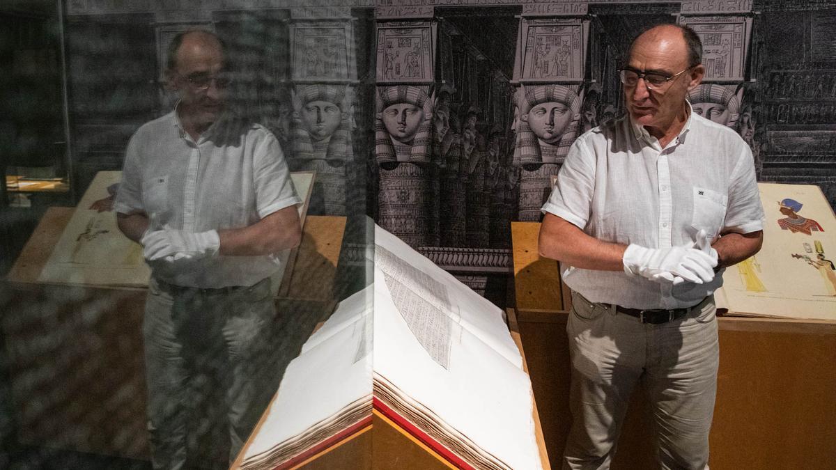 El conservador del Museu Egipci Luis Manuel Gonzálvez, señalando un antiguo libro de gran formato ligado a Champollion, ante la copia exacta de la piedra de Rosetta, este martes.