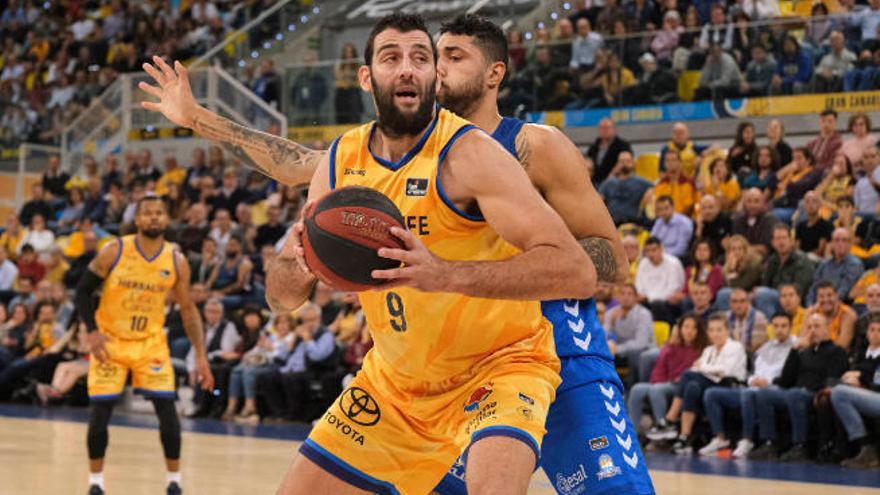 Ioannis Bourousis postea ante Augusto César Lima, del Burgos; mientras Omar Cook observa la jugada al fondo.