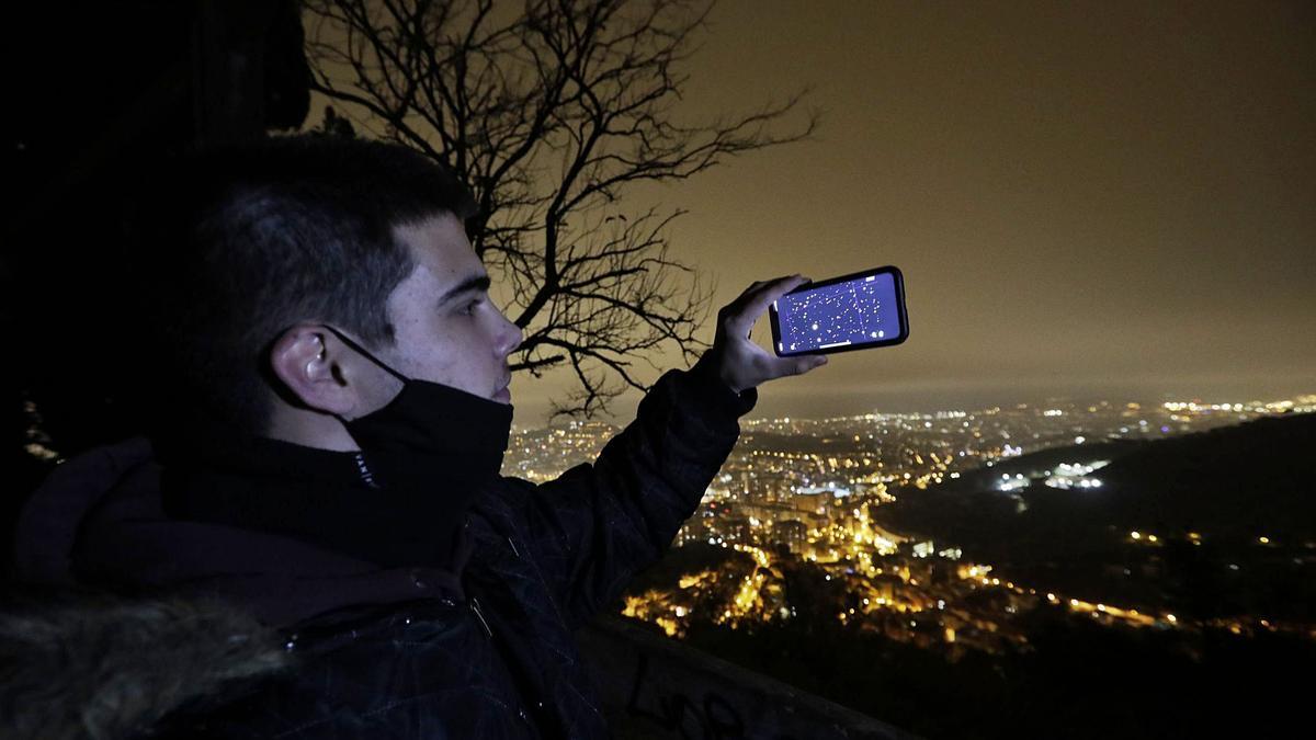 Un joven intenta localizar Júpiter y Saturno con una aplicación del móvil, esta semana, en Barcelona, aunque las nubes impedían su visualización.