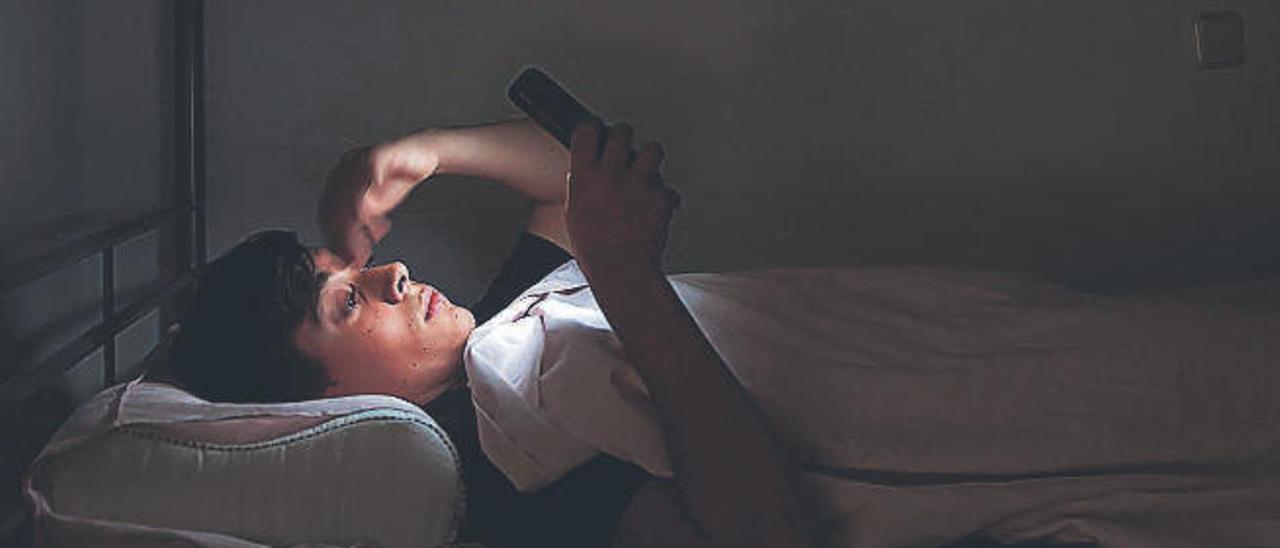 Un joven consulta su teléfono móvil en su dormitorio.