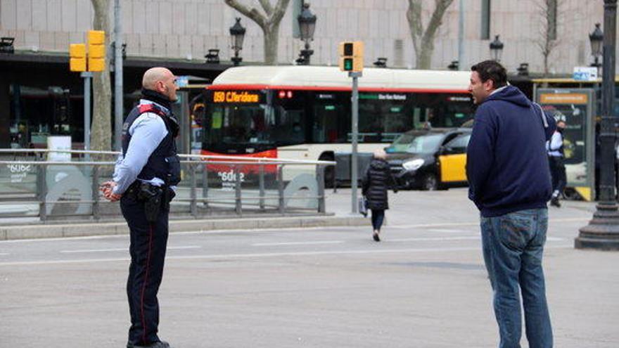 Un agent dels Mossos pregunta el destí i motiu del viatge a un vianant a la plaça Catalunya de Barcelona durant el primer dia laborable de l&#039;estat d&#039;alarma pel coronavirus.