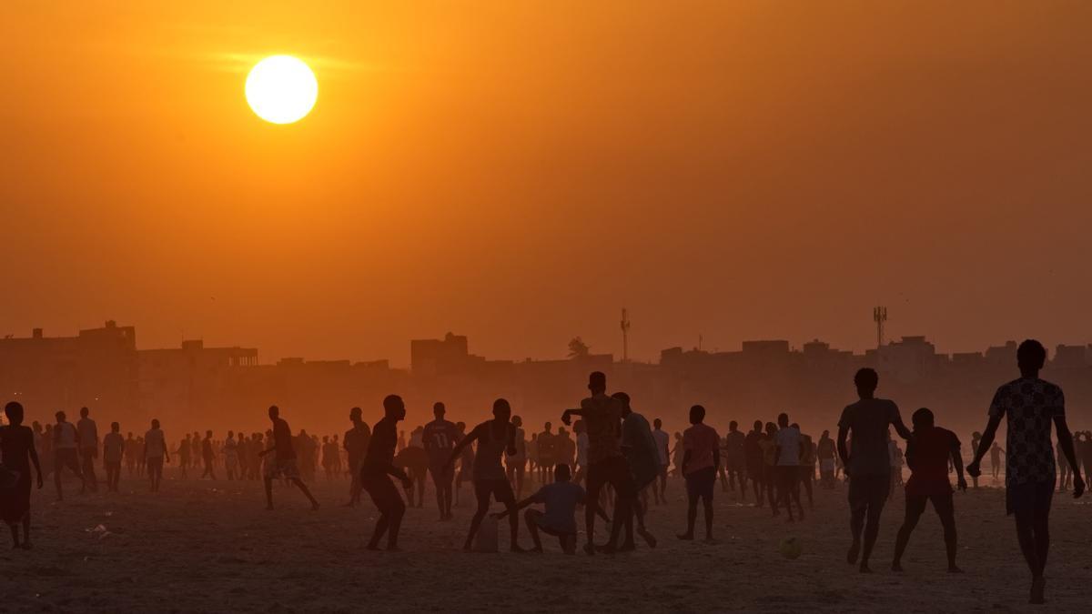 Decenas de jóvenes sobre la arena de la playa al atardecer.