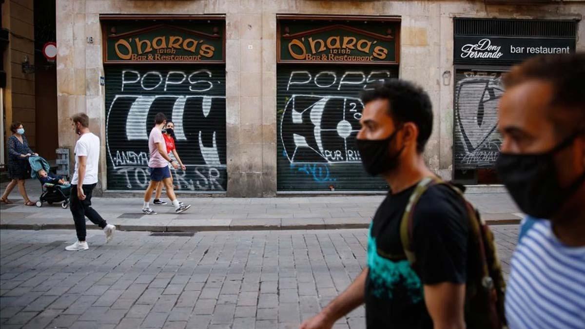 Consumo regulará los requisitos que debe cumplir una mascarilla higiénica. En la foto, dos hombres con mascarilla pasean por el centro de Barcelona, con los comercios cerrados.