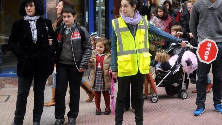 Una integrante del equipo de Camiños Escolares ayuda a un grupo de niños a cruzar una calle.  // R. V.