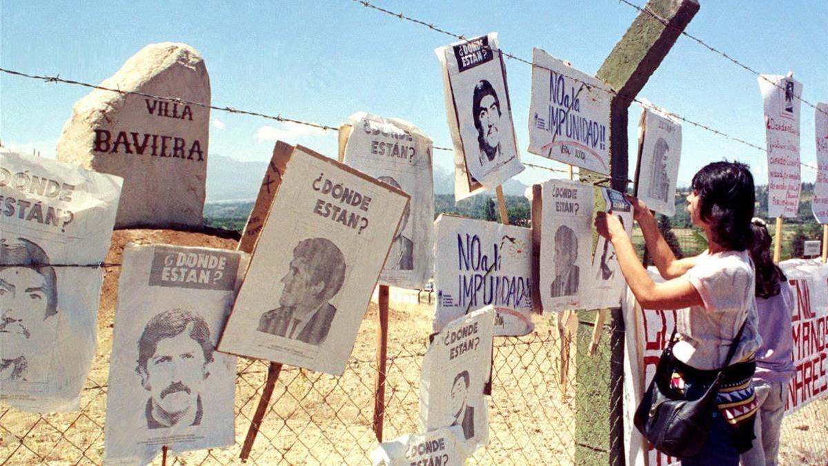 Una mujer cuelga carteles de chilenos desaparecidos en la cerca de Colonia Dignidad, que sirvió de centro de tortura de Pinochet.