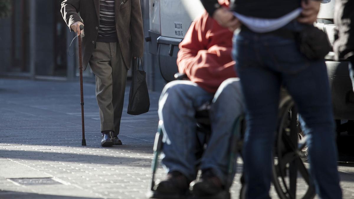 Un hombre con bastón se acerca a una persona en silla de ruedas