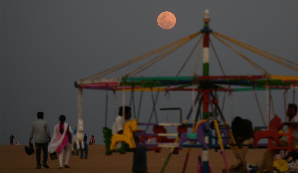 Una Super Luna de Nieve sale mientras los residentes disfrutan de la noche en la playa Marina en Madrás, India.