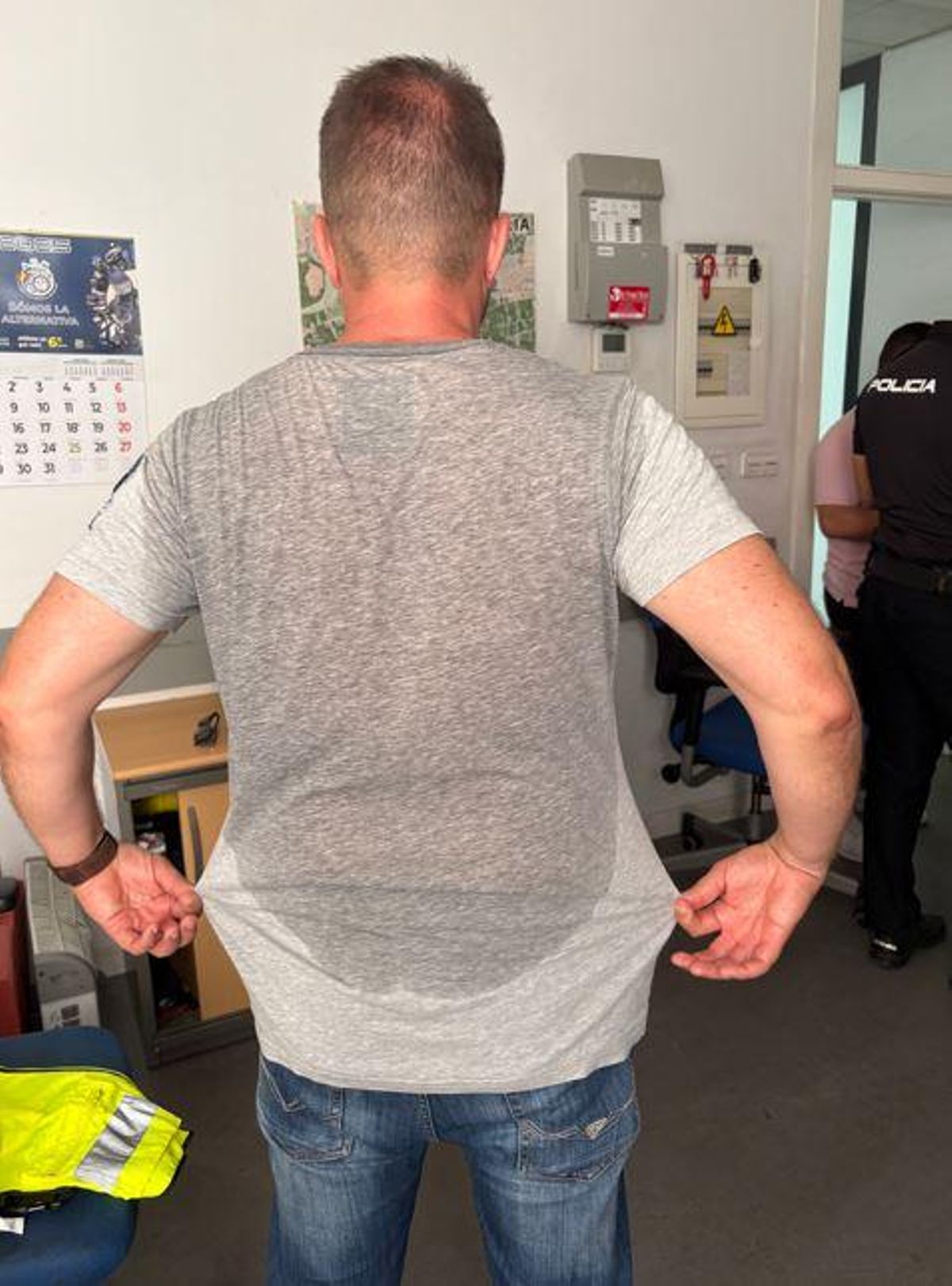 Un agente muestra su camiseta empapada de sudor.