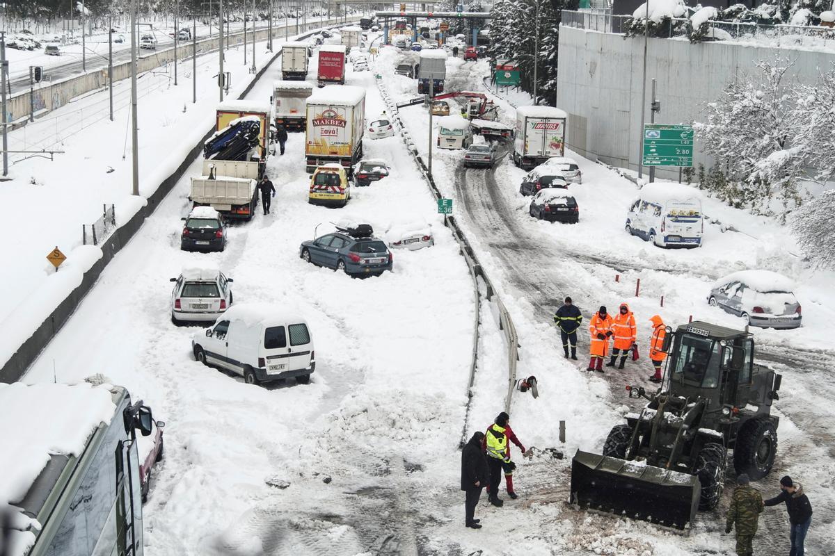 Un bulldozer del Ejército griego retira nieve en una carretera llena de coches varados, tras las intensas nevadas en Atenas.