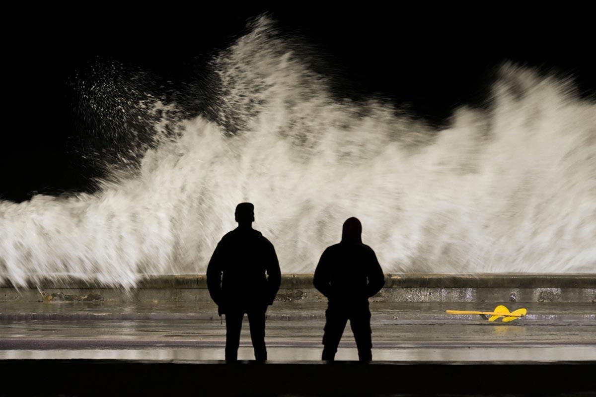 Cubanos observan las olas golpeando el Malecón de La Habana.