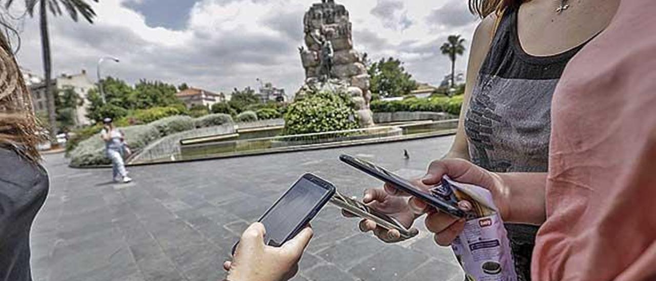 Tres jóvenes consultan su teléfono móvil en la zona wifi gratuita de la plaza de España, cuyos datos son almacenados para futuros usos.