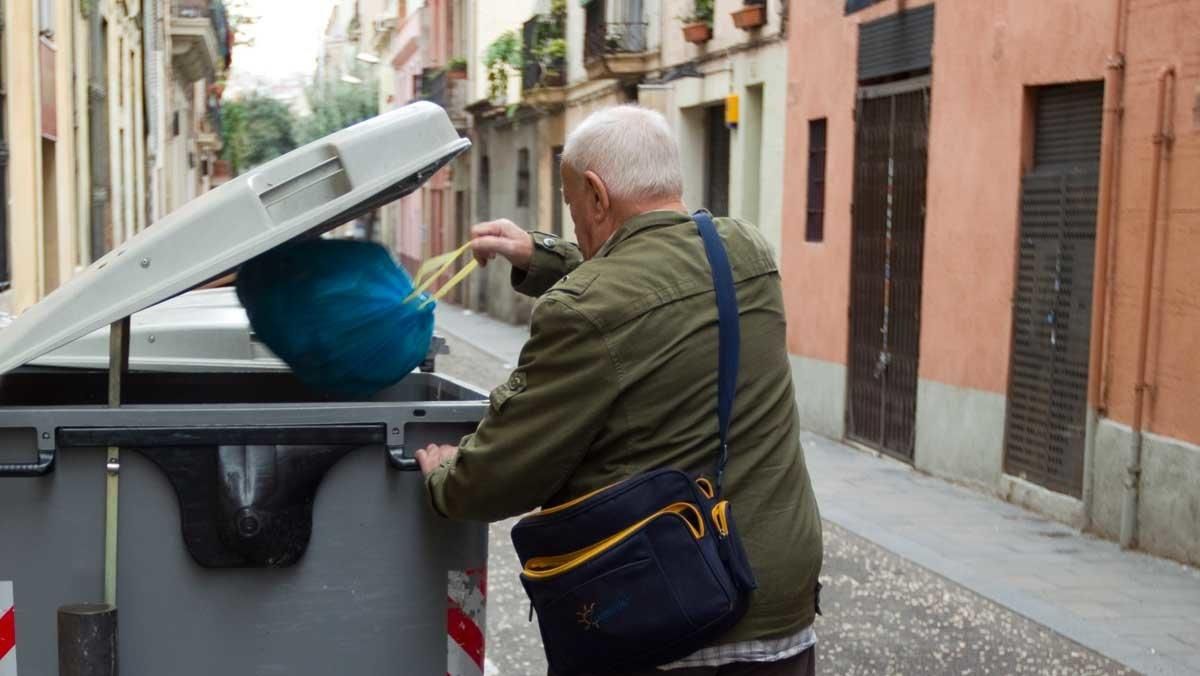 Un hombre tira una bolsa de basura en un contenedor de Barcelona.