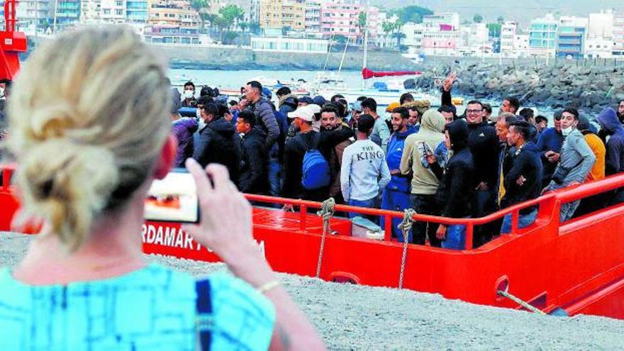 Una turista fotografía el desembarco de un grupo de migrantes en el puerto de Arguineguín, en Gran Canaria. | | REUTERS/ BORJA SUÁREZ