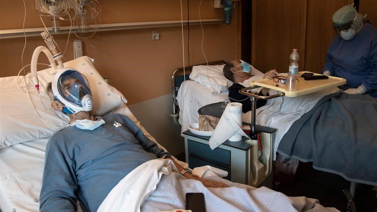 Un paciente con covid lleva una máscara de buceo integral en el Hospital Maria Pia de Turín, el 7 de abril del 2020, mientras su compañero de habitación está siendo atendido por un sanitario.