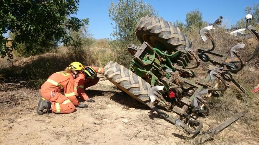 Los bomberos tratan de excarcelar el cadáver atrapado bajo el tractor.
