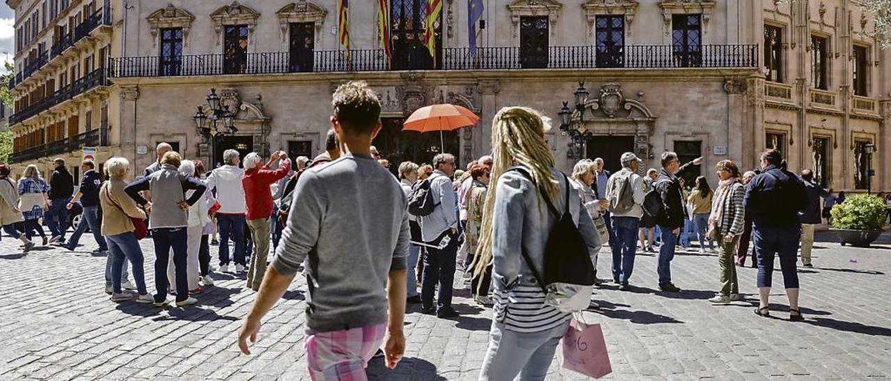 Un guía, sujetando un paraguas naranja, con un grupo de turistas en la plaza de Cort de Palma.