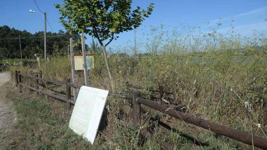 La zona de descanso, con un cartel abandonado, y la maleza cubriendo por completo un banco. // N.Parga