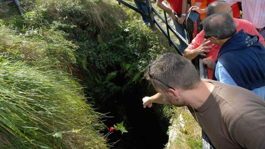 Un grupo de personas, lanzando flores al interior del pozo Funeres en uno de los actos de homenaje.