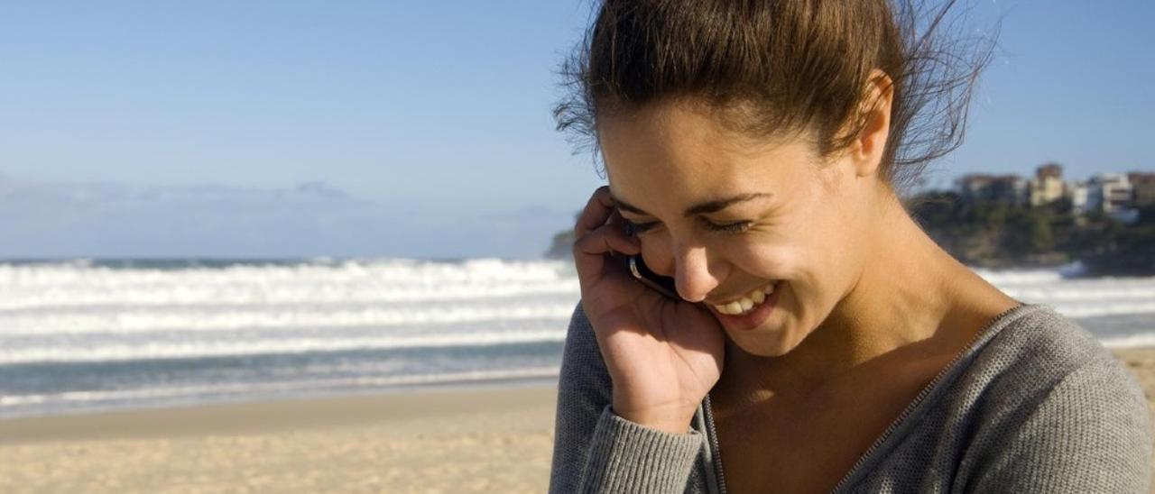 Una joven habla por teléfono en una playa.