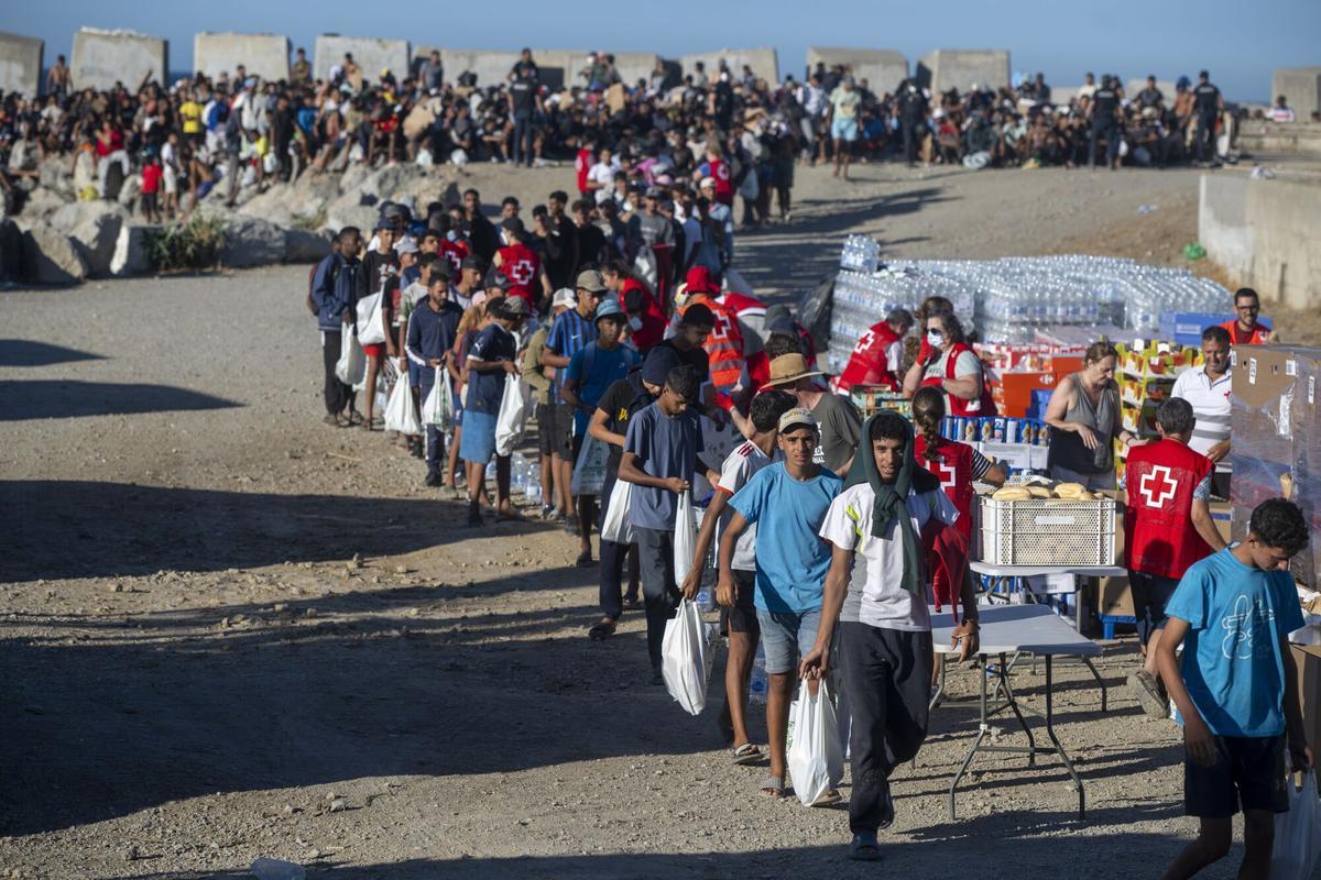 21/08/2026 Miembros de la Cruz Roja reparten comida a los inmigrantes en una playa, a 21 de agosto de 2026, en Ceuta (España). Ceuta sigue afrontando una grave crisis humanitaria después de la histórica entrada masiva de más de 70.000 migrantes a nado por el Tarajal durante los días 30 y 31 del pasado mes de julio. Aunque actualmente el despliegue policial y el refuerzo de la frontera por parte de las autoridades marroquíes han conseguido frenar las entradas, la ciudad autónoma sigue enfrentando una grave crisis humanitaria, sanitaria y de seguridad. POLITICA Marcos Moreno - Europa Press