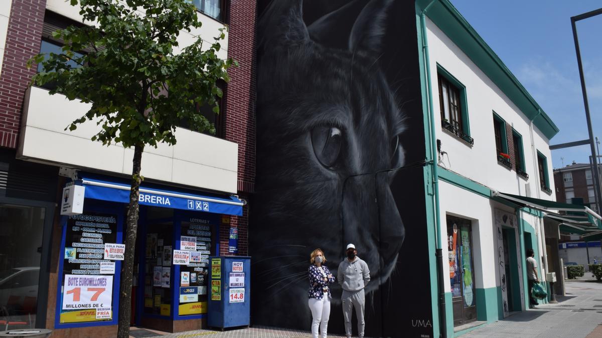 La edil Susana Madera, junto al artista valenciano &quot;Xolaca&quot;, en Lugones, ante el grafiti del gato negro