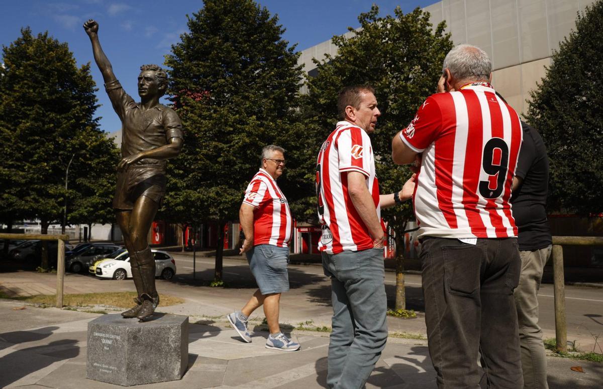 Aficionados del Sporting, ante la estatua de Quini en El Molinón. En el detalle, la portada de «Don Balón» donde Quini relataba su situación y el problema con el derecho de retención.  | JUAN PLAZA