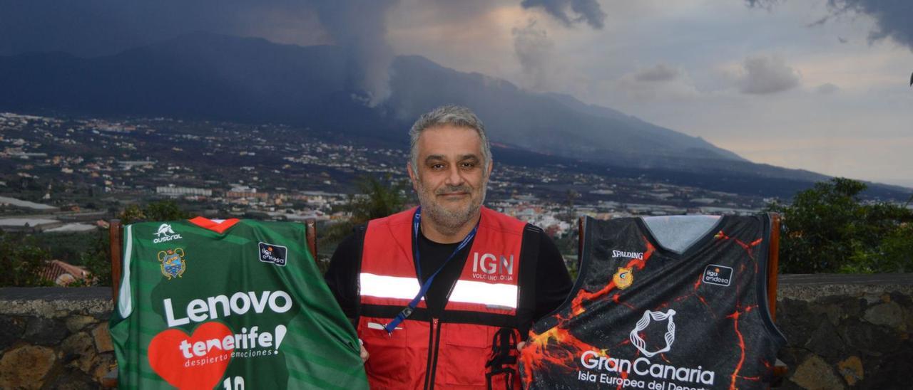 El geólogo Stavros Meletlidis posa con las camisetas volcánicas del CB Canarias –izqd.– y del CB Gran Canaria –dch.– desde el centro del IGN en La Palma. | | IAGO OTERO