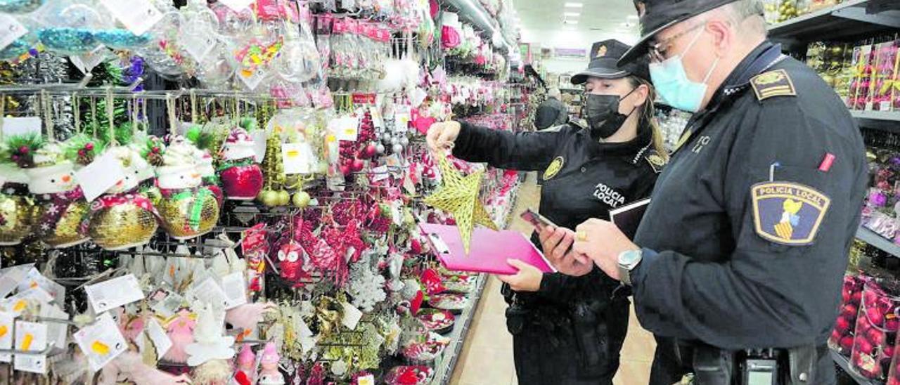 Dos agentes de la Policía Local inspeccionan adornos navideños en un comercio para comprobar que cumplen la normativa. | ANTONIO AMORÓS