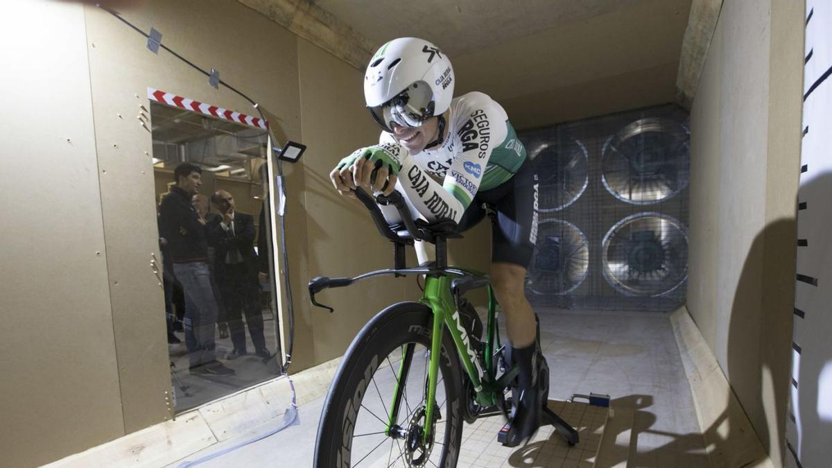 El ciclista Jonathan Lastra prueba el túnel de viento mientras Chechu Rubiera y el Rector lo observan desde fuera, en las instalaciones de la Escuela Politécnica de Mieres. | Miki López
