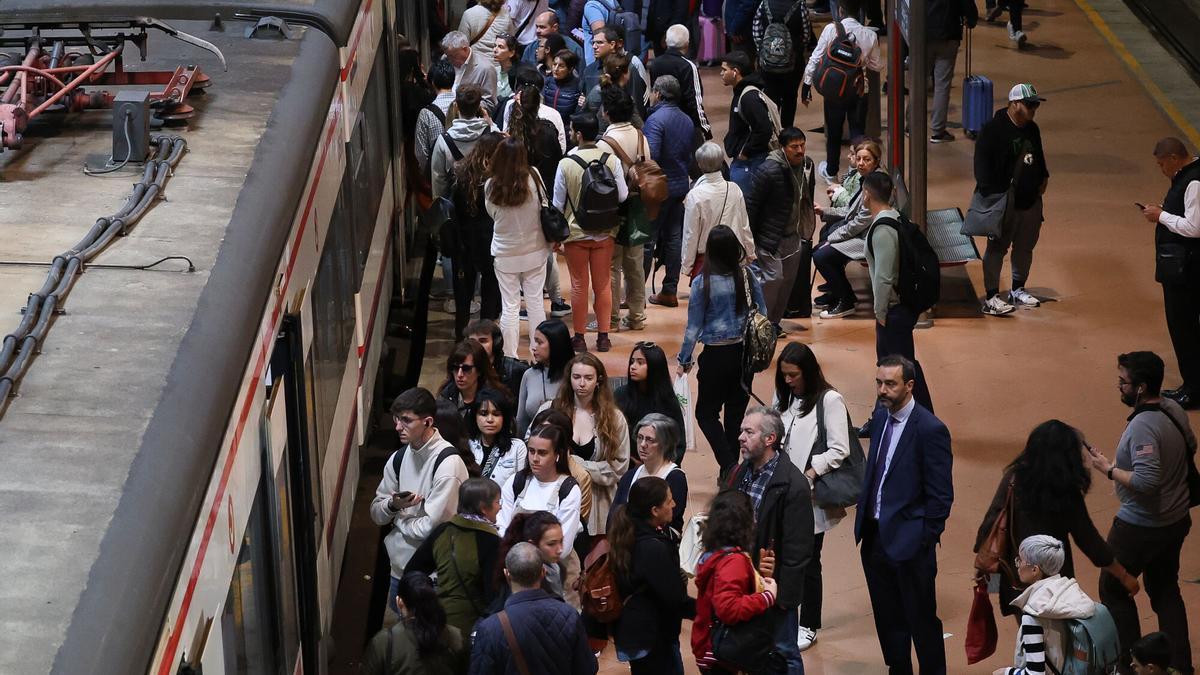 Numerosas personas con maletas esperan en el andén la salida de un tren.