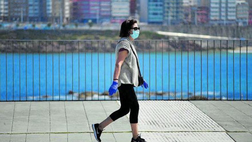 Una mujer, en el paseo marítimo de A Coruña, con mascarilla y guantes. |   // CARLOS PARDELLAS