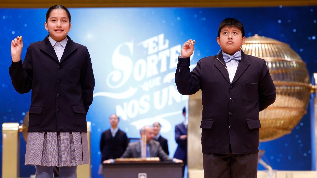 Los niños de la Residencia San Ildefonso de Madrid Piero Rai Chávez (d) y Alisce Ríos (i), muestran el número 45.456, otro quinto premio dotado con 60.000 euros a la serie, durante el sorteo de la Lotería de Navidad que se celebra este domingo en el Teatro Real, en Madrid.