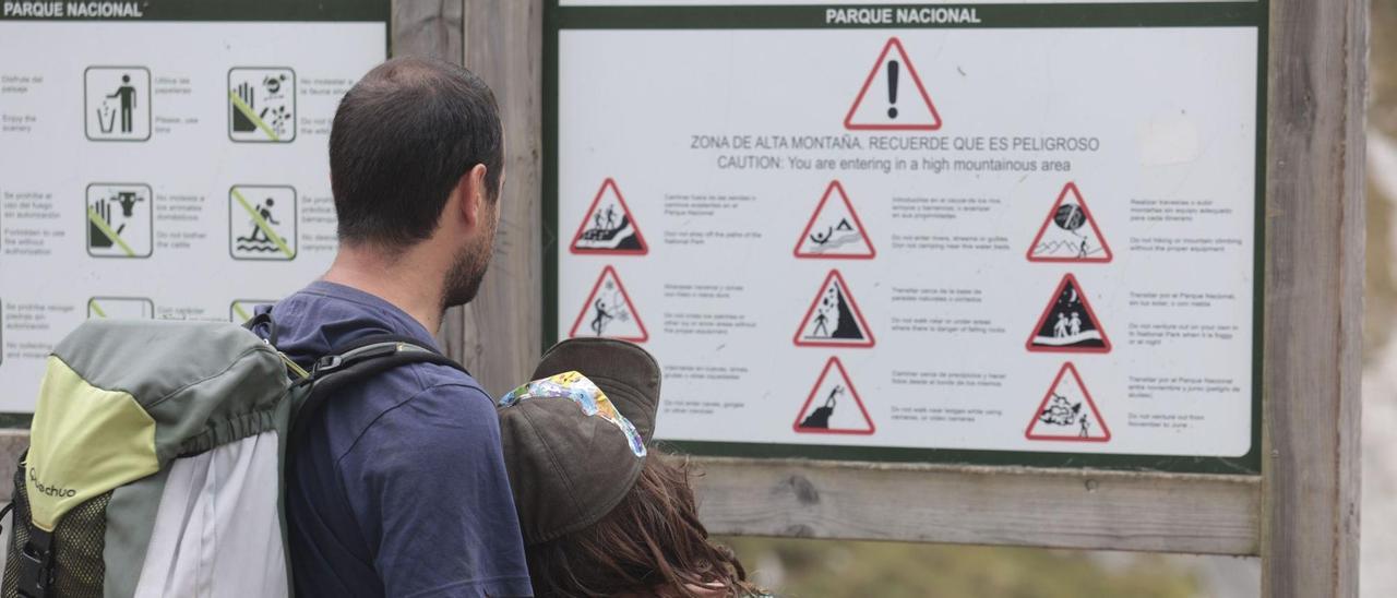 Un padre y su hija leen un cartel que advierte de los riesgos de los Picos de Europa