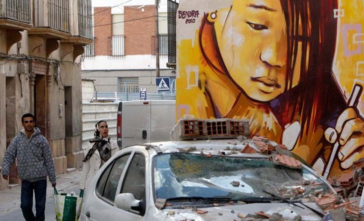 Dos veïns de Llorca passen davant un cotxe destrossat pel terratrèmol que ha afectat la localitat murciana.