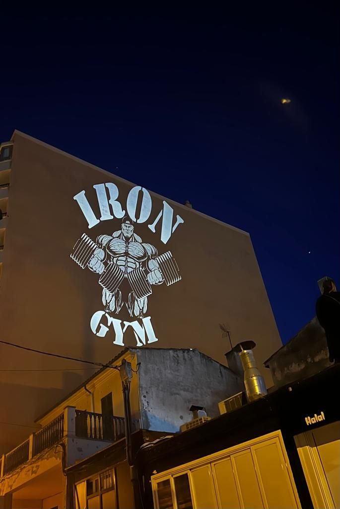 Mit einem auf eine Hauswand projizierten Logo des Iron Gym wollen die Auswanderer um Kunden werben.