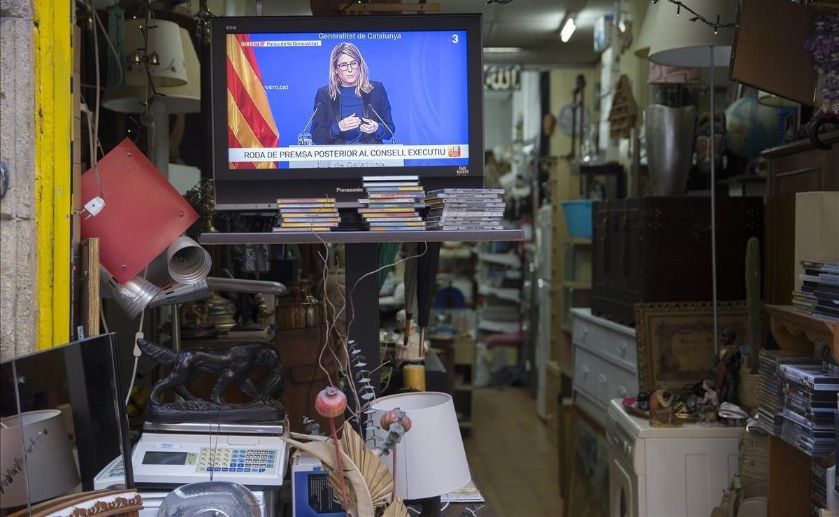 Un televisor emite la rueda de prensa de la consellera de presidencia y portavoz del Govern, Elsa Artadi, en una tienda de segunda mano, en la calle Riera Alta, de Barcelona.