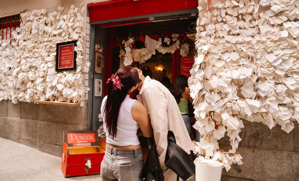 Una pareja se besa frente los deseos colgados en la fachada de Peque Story.