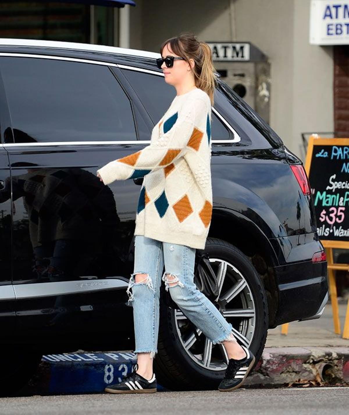 Dakota Johnson con jersey de rombos, pantalones vaqueros y zapatillas Adidas