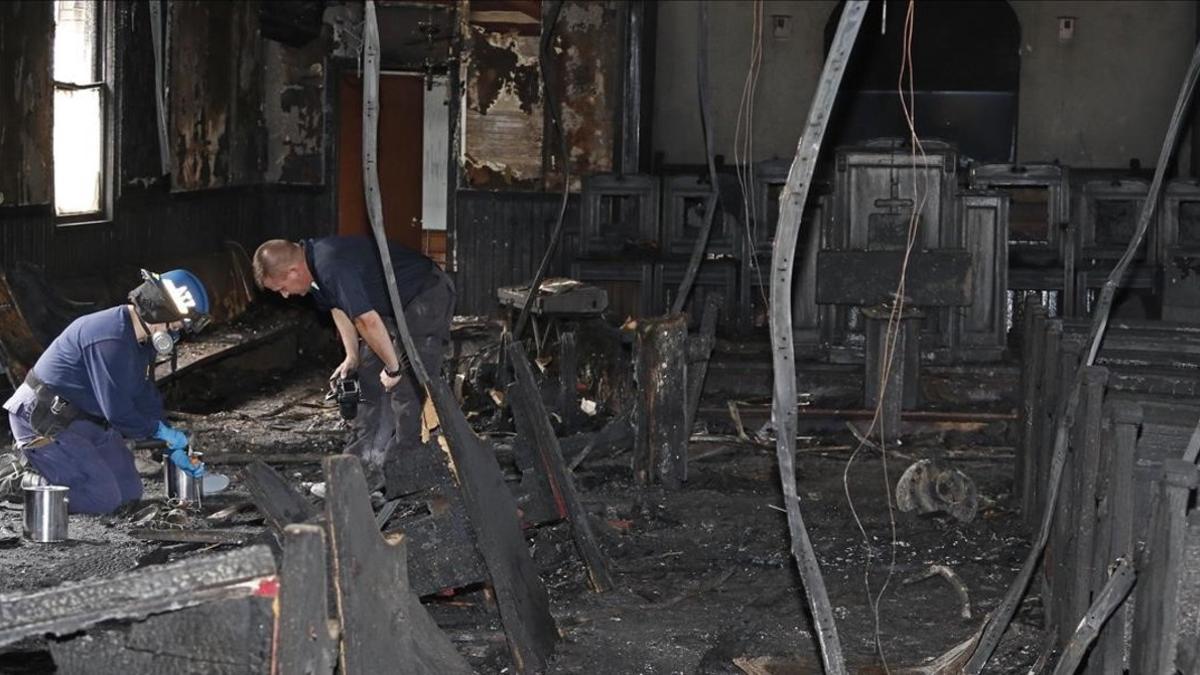 Un agente de policía y un bombero buscan pistas entre los escombros de la iglesia incendiada.