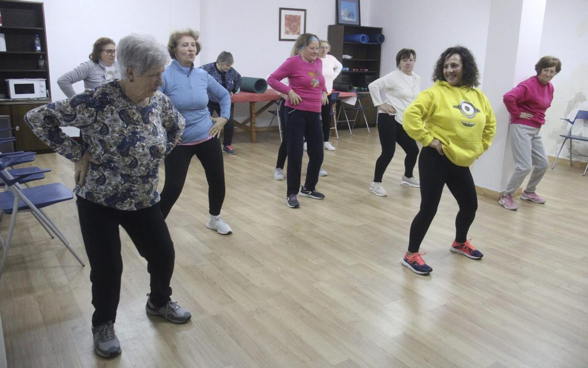 La monitora María José Hernández (sudadera amarilla) dirige a varias mujeres de Requejo durante la clase de gimnasia. Abajo, trabajo con mancuernas.  | ARACELI SAAVEDRA