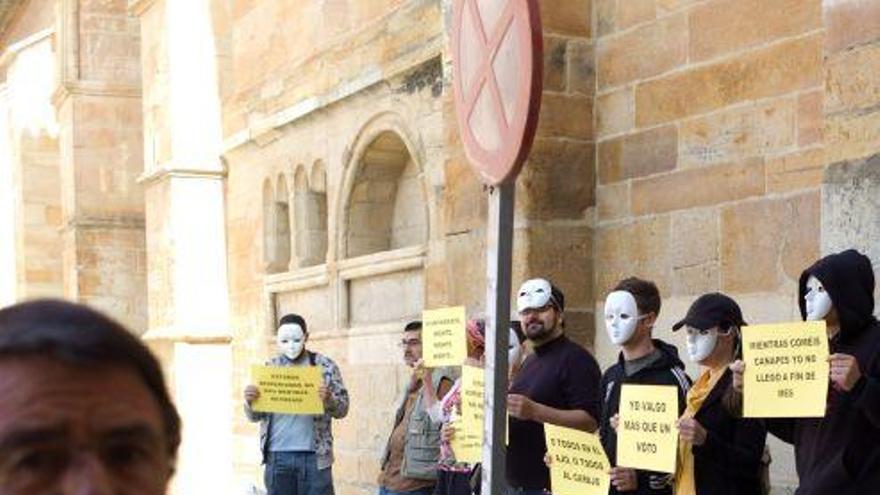 Mañanes, antes del pleno, pasa junto a los miembros del M-15 con caretas blancas y pancartas.