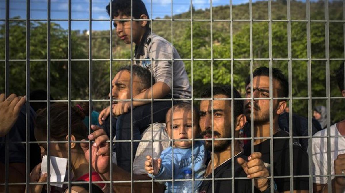 Refugiats i immigrants esperen rere una reixa, en un camp de futbol, a poder ser registrats, a Mitilene, aquest dimarts.