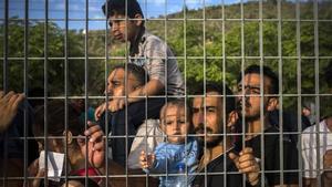 Refugiados e inmigrantes esperan tras una verja, en un campo de fútbol, a poder ser registrados, en Mitilene, este martes.